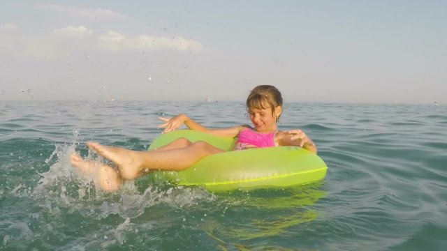 A happy child splashing into the sea. The girl in the inflatable circle makes a splash with her feet.