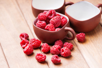 Raspberries in a cup and on a wooden table 