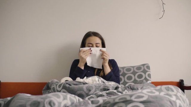 Young woman blowing nose in paper tissue in the bed