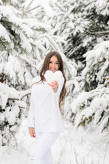 girl in a white warm sweater in a winter forest holds a heart from the snow