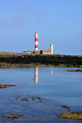 Leuchtturm mit weiß und roten Streifen und sein Spiegelbild im ruhigen Wasser.
