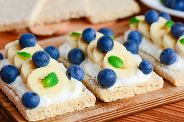 Crispbread toast with cottage cheese, banana and berries on wooden board. Cottage cheese open sandwich idea. Closeup