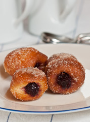 Jelly filled brioche donut hole /  three freshly baked, warm Jelly filled brioche donut holes on a white, round plate with a blue rim on a white table cloth with thin blue stripes 