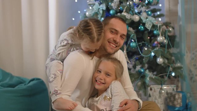 Happy father with two daughters laughing, playing and hugging near Christmas tree