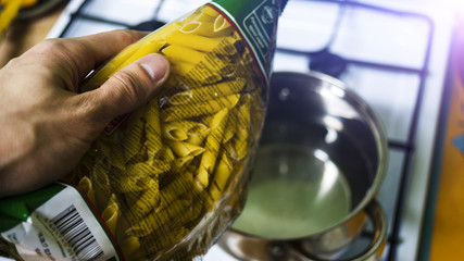 Man's hand with packing pasta at the pot with water concept cooking food