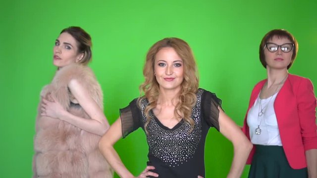 Three beautiful young women in stylish clothes dansing at camera on green screen background