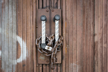 Padlock and chain locked securely on rusty door.
