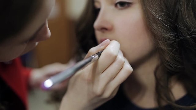makeup artist paints lips to the teenager girl in the beauty salon