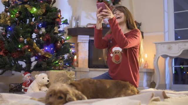 Beautiful girl photographs her dog near Christmas tree