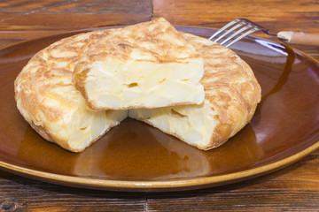 Tortilla española con patatas con un trozo cortado, sobre un plato de barro 