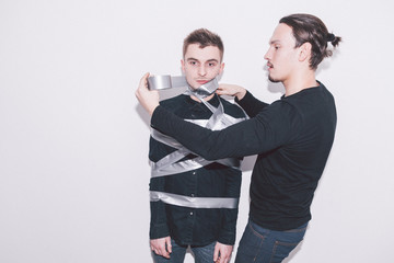 boy winding another boy with a touch grey scotch tape up to his face
