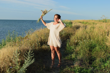 young Slavic girl in a white dress and with flowers, enjoys life against the sea