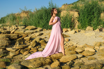 beautiful young girl with gathered hair in a long dress is walking along the seashore. Beautiful legs