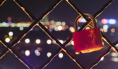 Red padlock with heart shape on it in front of the city lights. Romantic scene.