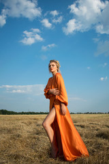 Beautiful and passion woman with sexy legs in a long orange dress in the field.  Sexy blond girl with amazing legs on tha background of the field
