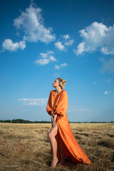 Beautiful and passion woman with sexy legs in a long orange dress in the field.  Sexy blond girl with amazing legs on tha background of the field