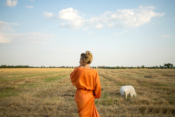 Beautiful woman in a long orange dress with white dog in the field. Samoyed