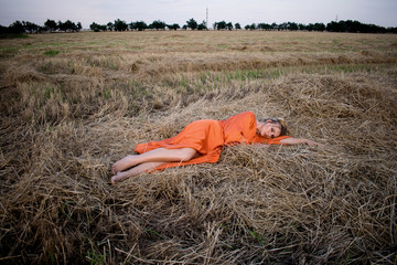 Beautiful blonde in a long dress with beautiful legs lies in a field on a hay