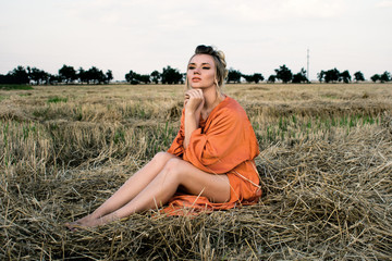 Beautiful smiling blonde with elegant long legs in a long orange dress in the field