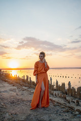 Passion woman with beautiful long legs in a long orange dress at sunset