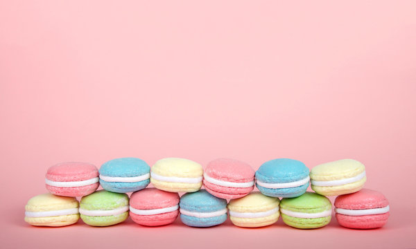 Large Macaroon cookies covered in granulated sugar on a table, two rows stacked alternating colors. pink background. Popular pastry in France.