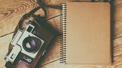 Old retro camera,  spiral blank kraft paper notebook on vintage rustic wooden planks boards. Education photography courses back to  school concept abstract background. Close up, top view, horizontal.