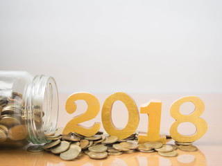 New year saving money and financial planning concept. Coins spilling out of glass bottle w/ gold wooden number 2018 on table. Idea for business growth, tax payment, investment and banking. Copy space.