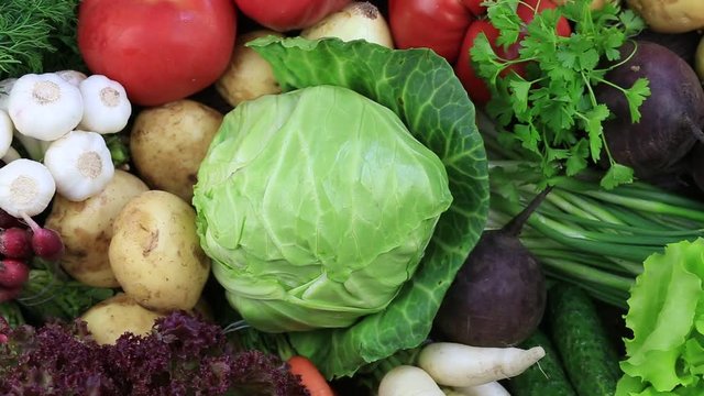 Assortment of fresh raw vegetables arranged on a rustic wooden table tray. Selection includes carrot, potato, cucumber, tomato, cabbage, lettuce, beetroot, onion, garlic, radish, dill and parsley