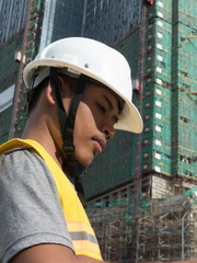 Asian architect profile looks down at plans with large housing project under construction in background