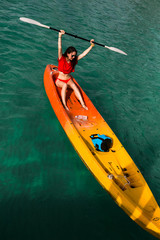 Fototapeta premium Brunette young woman girl in red bikini paddling on red, orange, yellow kayak in the blue water. Asia. Thailand