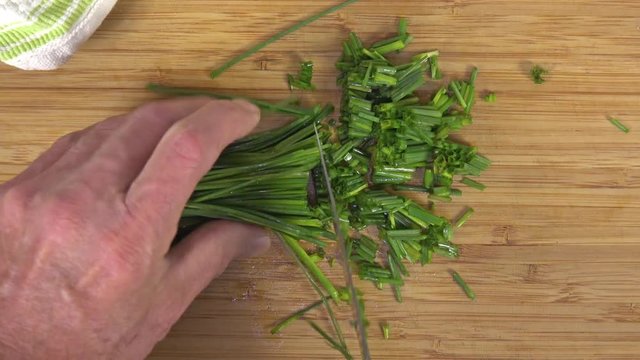Overhead view of chopping fresh chives on a cutting board