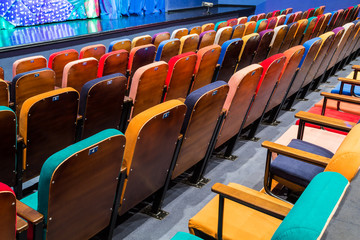 The auditorium in the theater. Multicolored spectator chairs. The stage with scenery and curtains.
