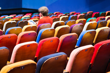 The auditorium in the theater. Multicolored spectator chairs. One person in the audience.