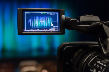 The LCD display on the camcorder. Videography in the theater. Blue-green curtain on the stage.