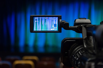 The LCD display on the camcorder. Videography in the theater. Blue-green curtain on the stage.