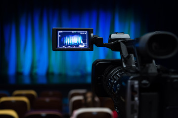 The LCD display on the camcorder. Videography in the theater. Blue-green curtain on the stage.