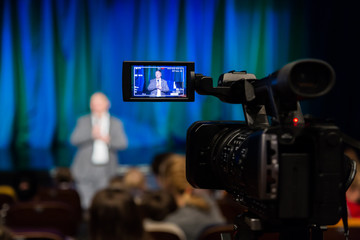 The LCD display on the camcorder. Shooting event. A man stands in front of an audience. The TV...