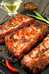 A black glass plate of juicy smoked bbq spareribs with red peppe