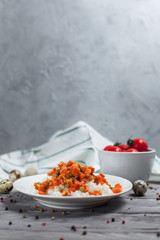 Fototapeta na wymiar tasty rice with stewed carrots, peas and onions on a white plate, quail eggs, bowl with cherry tomatoes, pepper and towel on a light wooden table on a light gray background