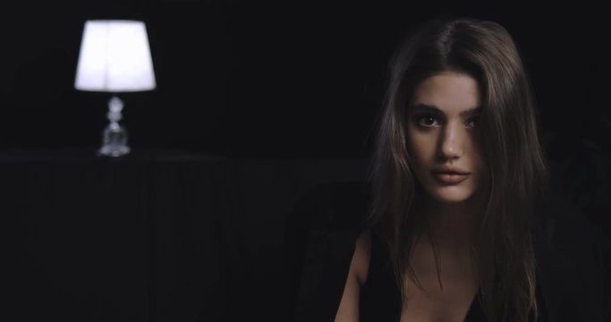 Attractive brunette sexy woman (girl) with nice makeup looking up to the camera on the black background, lamp in out of focus, soft light, portrait