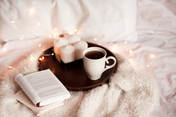 Open books, candles and cup of tea on wooden tray in bed. Good morning. Leisure time.