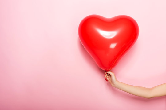 Female hand holding a red ball in the shape of a heart, isolated on a pink background.