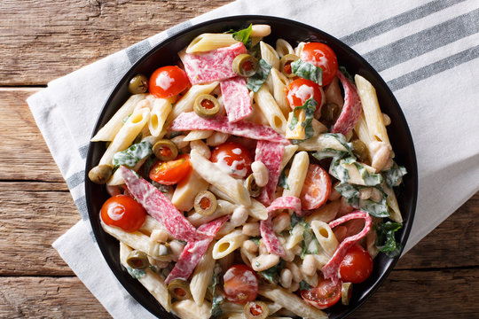Italian food: penne pasta with salami, cheese, and vegetables close-up. Horizontal top view