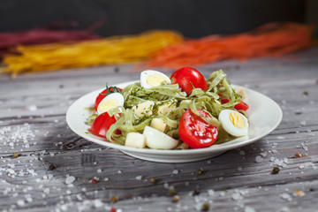 pasta from green spinach with mozzarella, greens and French mustard, quail eggs and cherry tomatoes on a plate, bell pepper and large sea salt on a gray wooden table on a dark background
