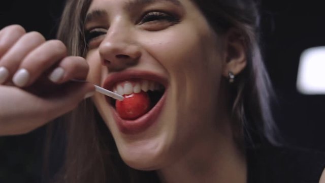 closeup portrait of amazing sexy brunette putting orange lollipop in her mouth, laughing