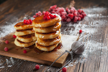 syrups with powdered sugar on a wooden cutting board, a sieve of a viburnum berry and caramel topping on a dark wooden table