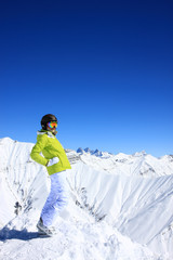 Sport girl in helmet and sun glasses mask and ski boots portrait with white snowy mountains background and deep blue sky at the mountains ski resort. Active lifestyle. Georgia, Gudauri, Caucasus