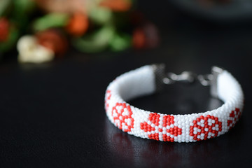 White bracelet with red flowers on a dark background close up