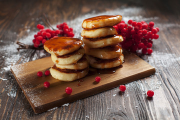 syrups with powdered sugar on a wooden cutting board, a sieve of a viburnum berry and caramel topping on a dark wooden table