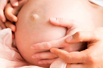 two pairs of hands on the bare belly of a pregnant woman